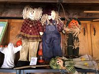 Top shelf with large scarecrow dolls, pumpkin figure, ghost figurine, lying doll