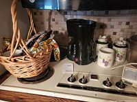 Photo of coffee pot, grape-themed ceramic canisters, and utensil basket on stove