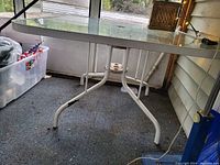 Glass vintage patio table from side angle showing metal legs and glass top with umbrella hole.