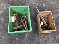 Overview of two containers - a green plastic tub holding barn door hinges and metal hardware, and a wooden box holding rusted metal chains and bars.