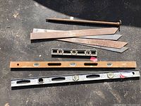 View of 4 steel straight edges, two carpenter levels (wood and metal), and 18-inch level laid on pavement showing size and condition