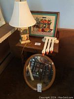 Wooden box with oval mirror resting against it, table lamp with duck decoration on the base, and framed stitched duck art behind