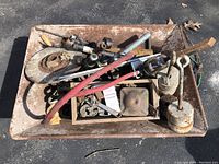 Top view of rusty metal cement mixing pan containing assorted rusty metal parts including pipes, adjustable wrench, red hose, and weights