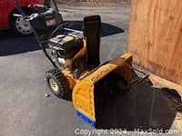 Front-side view of yellow snow thrower showing auger housing, black chute and pneumatic wheels.
