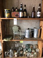 Three wooden shelves displaying vintage beer bottles on the top two shelves, including a pack of diamond brand beer bottles, various other bottles, an aluminum double cooker pot and pitcher on the middle shelf, and a collection of vintage spice jars and Ball canning jars on the bottom shelf.