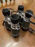 Side view showing two pairs of black and chrome binoculars with adjustable focus knobs and attached neck straps.