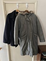 Two coats hanging on wall hooks showing overall length and style difference