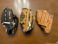 Three children's baseball gloves placed on a wooden surface showing different colors and designs.