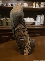 Front angled view of the wood carving featuring the stylized Indigenous face and natural texture of alder wood with visible carved lines.