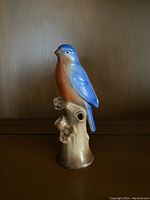 Front and side views of the ceramic bluebird figurine on a tree branch perch showing color and glossy finish.
