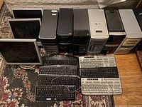 Wide shot showing 6 desktop towers, 3 monitors, and 7 keyboards laid out on floor and carpet