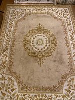 Photo showing the full view of the rectangular beige wool rug with floral central medallion and border.