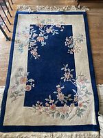 Full flat view of the rectangular handmade Chinese wool rug with floral designs and fringed edges.