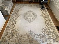 Full view of large rectangular Indian floor rug with central medallion pattern and ornate floral border on off-white background, showing wear and some spots.