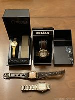 Photo showing four wristwatches including Caravelle by Bulova in box, Orléan in box, and two others on table with leather and metal straps.