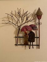 Full view of metal art depicting couple under umbrella beside street lamp and tree with twisting branches.