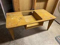 Angled front view of the vintage mid-century rectangular coffee table with tapered legs and surface wear.