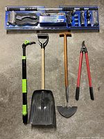 Photo displaying all the outdoor tools including brushes, shovel, spade, pruners, hose sprayer, and garden tool lined up on grey surface