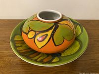 Top and side view of Poole ceramic vase resting on matching ceramic bowl, showing orange and green floral and abstract painted design.