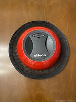 Top view of the Vileda Virobi Robot Sweeper device showing its round shape, red and black colors, and brand logo.