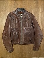 Front view of brown leather jacket laid flat on wooden floor