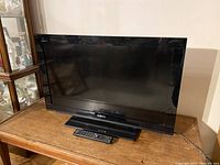 Sony LCD digital colour TV Model KDL-32BX320 on wooden table with remote control visible on the base stand.