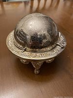 Closed roll-top butter dish showing engraved dome lid and ornate legs.