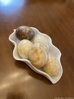 Five decorative stone eggs arranged in a white plastic bowl from a top angle showing color variations and bowl shape.