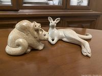Two stoneware animal figurines on a wooden surface: a resting kangaroo and a koala bear with baby on its back.