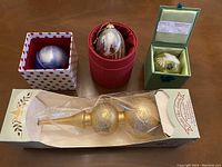 Three boxed Li Bien Christmas ornaments displayed alongside a boxed gold glass ornament tree topper
