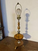 Full view of the vintage table lamp showing amber glass body, wooden neck and base, and metal socket without lampshade