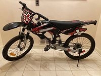 Side profile showing entire bike with black and red graphics, knobby tires, and cushioned seat.