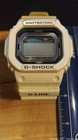 Front view of white Casio G-Shock G-Lide digital watch on a wooden surface with a ruler for size reference.