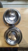 Two stainless steel dog bowls placed on a wooden surface showing interior wear marks.