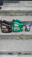 Three bottles of motor oil placed on outdoor concrete steps: Castrol EDGE 5W-30, Castrol GTX 10W-30, and Mobil Super 5W-30.