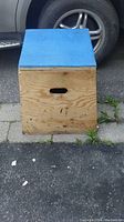 View of wooden plyo box front side showing blue padded top and handle cut-out on side near ground.
