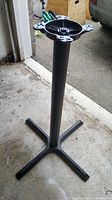 Black metal table base standing on a concrete floor. The base is 41 inches tall with a round mounting plate on the top and four legs at the bottom for stability.