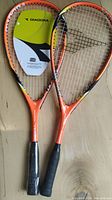Two orange-framed junior squash racquets with black grips, one with protective Diadora face sheet