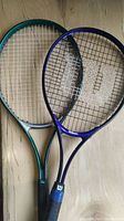 Photo showing two tennis racquets placed side by side on a wooden surface, Wilson on the right and Dunlop on the left
