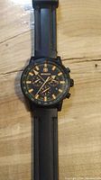 Front view of Wenger black chronograph watch with black rubber strap showing dial with orange accents.