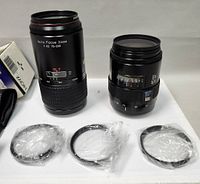 Two vintage zoom camera lenses standing upright with three circular lens filters in plastic wrappers laid out in front.