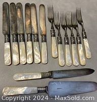 Six mother-of-pearl handle knives and six matching four-tine forks arranged with one additional knife and protective sheath