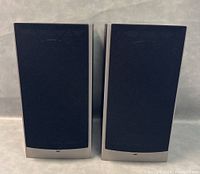 Pair of Athena Technologies AS-B2.2 speakers front view with black fabric grills attached, silver bottom trim and rectangular shape.