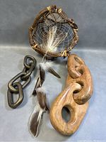 Photo showing dreamcatcher with natural wood frame, feathers, dark metal chain and wooden carved chain side by side on a blue-grey surface