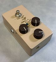 Top angled view showing three knobs, footswitch, and LED indicator on beige enclosure with faded graphics