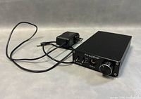 Front angled view of the Fx-Audio DAC-X6 digital audio decoder with attached power adapter.