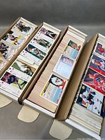 Four long cardboard boxes filled with hockey cards showing front and back sides of various players in uniform.
