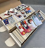 Two open cardboard boxes filled with large quantities of hockey cards. A few cards laid on top show detailed front images of hockey players.