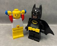 Pair of LEGO night lights showing the Batman figure with detailed facial expression and the classic yellow LEGO minifigure, both standing with raised arms and good condition, photographed against a plain background.