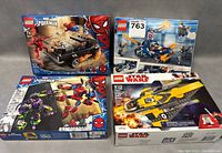 Four LEGO sets placed together on a gray surface with visible front view of boxes including Spider-Man and Star Wars themes.